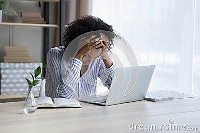 Depressed upset black female sit at workplace hug head Stock Photo