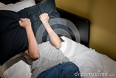 Depressed woman covering her face with black pillow and screaming Stock Photo
