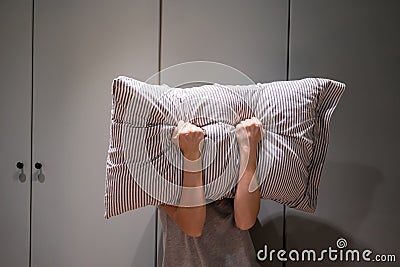 Depressed woman covering her face with pillow and screaming Stock Photo