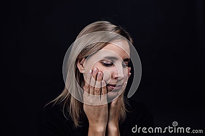 Depressed woman face with hands touching cheeks wearing black dress on black background. Victim of physical and Stock Photo