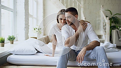 Depressed yong man sitting in bed having stressed while his girlfriend come and embrace him and kiss in bedroom at home Stock Photo