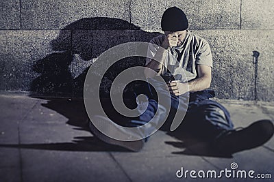 Depressed young man sitting on street ground with shadow on concrete wall Stock Photo