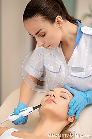 Dermatologist wearing blue gloves while cleansing skin for client Stock Photo