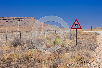 Desert landscape view of a sharp left turn sign on a dirt road i Stock Photo