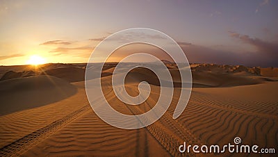 Desert at sunset hour with dune buggy tires tracks in the sand in the foreground. Stock Photo