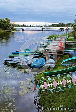 Deserted boat station in the evening. Jetty by the water, lifebuoys and boats at dusk Stock Photo