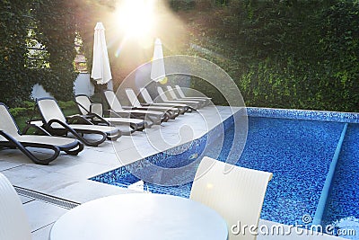 Deserted pool and sun loungers by the pool in the gentle rays of the morning sun. Place of rest and relaxation, Stock Photo