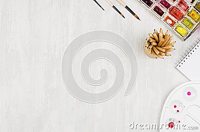 Designers workplace - stationery for creativity - watercolor paints, palette, brushes, colored pencils on white wood table. Stock Photo