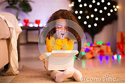 Amazed little afro girl opening Christmas gift near xmas tree Stock Photo