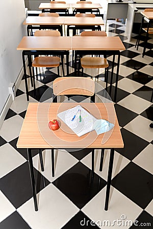 Desk with an apple, medical mask and a copybook in an empty classroom, new normal, back to school during Covid-19 Stock Photo