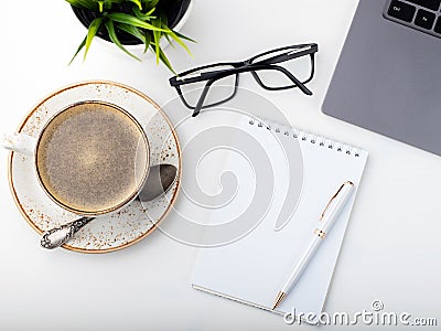 Desk with laptop, eye glasses, notepad, pen and a cup of coffee on a white table. Top view. Flat lay. Light background Stock Photo