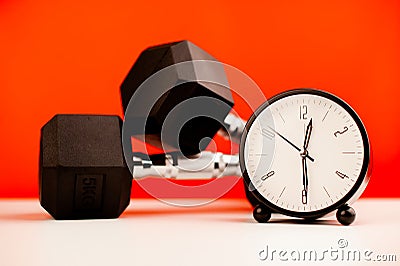clock on desk side by side with dumbbells for exercise during work time fitness concept Stock Photo