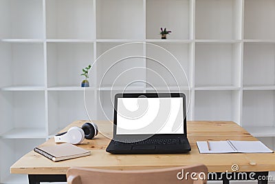 Desk table with laptop, headphone, notepad with white bookshelf Stock Photo