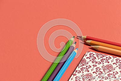 Desktop in vivid coral with notebook in the corner and color pencils Stock Photo