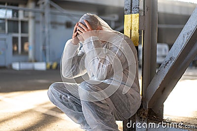 Despair healthcare worker in white covid protective overalls. Tired Male caucasian doctor grabs his head cower in depression Stock Photo