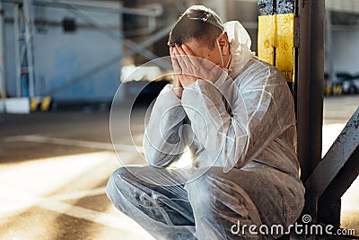 Despair healthcare worker in white covid protective overalls. Tired Male caucasian doctor grabs his head cower in depression Stock Photo