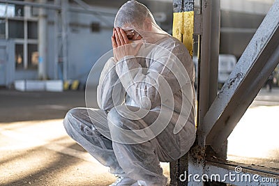 Despair healthcare worker in white covid protective overalls. Tired Male caucasian doctor grabs his head cower in depression Stock Photo