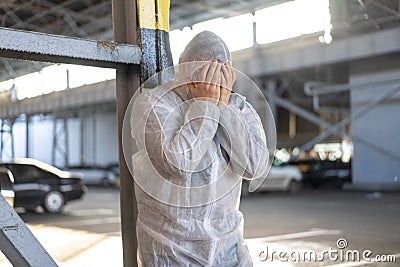 Despair healthcare worker in white covid protective overalls. Tired Male caucasian doctor grabs his head cower in depression Stock Photo