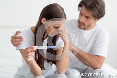 Despaired sad millennial european husband calms, support his wife, lady hold pregnancy test Stock Photo