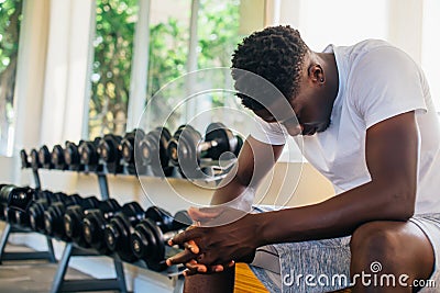 Desperate African American man sitting on bench during break in fitness training in modern gym Stock Photo