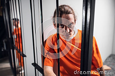A desperate criminal maniac with tattoos in a solitary cell is kept behind bars. A hard look at the camera. Stock Photo