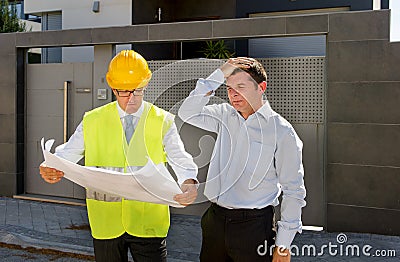 Desperate customer in stress and constructor foreman worker with helmet and vest arguing outdoors on new house building blueprints Stock Photo