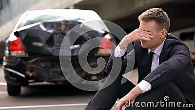 Desperate man sitting asphalt on crashed car background, automobile accident Stock Photo