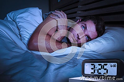 Desperate man in stress sleepless on bed with eyes wide opened suffering insomnia sleeping disorder depressed with digital alarm Stock Photo