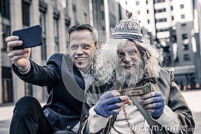 Desperate poor old man kissing dollar bill while smiling man making photo Stock Photo