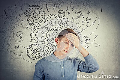 Desperate teen boy covering his forehead with hand. Hopeless situation, hard thinking as cogwheel gear brain arrows and mess Stock Photo