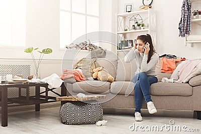 Desperate woman sitting on sofa in messy room Stock Photo