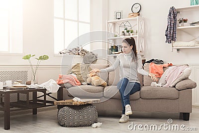 Desperate woman sitting on sofa in messy room Stock Photo