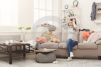 Desperate woman sitting on sofa in messy room Stock Photo