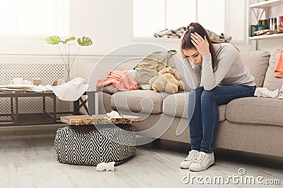 Desperate woman sitting on sofa in messy room Stock Photo