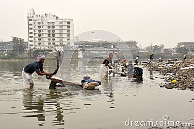 Dirty Laundry: Washerman wash clothes in polluted water Editorial Stock Photo