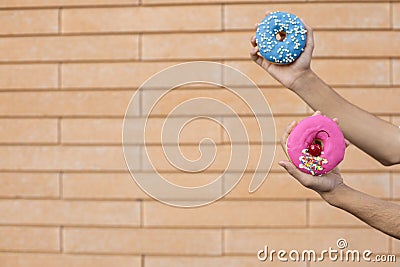 Close-up of a pink doughnut with red cherry and sprinkle glaze and a blue donut with beads held by an american male hand Stock Photo