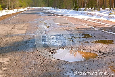 Destroyed broken asphalt road with holes, melting snow and puddles early spring. Stock Photo