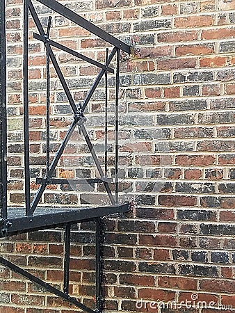 Detail of Decorative Wrought Iron Urban Fire Escape Against a Red and Black Brick Wall Stock Photo