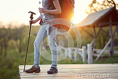 Detail of female backpacker finishing her hiking at sunset in nature, holding bottle of water and walking stick. healthy living, Stock Photo