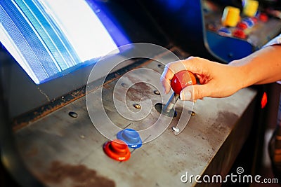 Detail on a hand holding joystick close to blue and red button controls of an old vintage arcade video game Stock Photo