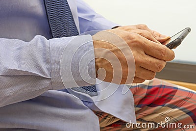 Detail of Hands of a man using a mobile phone and wearing a dress with a shirt, tie and pajama Stock Photo