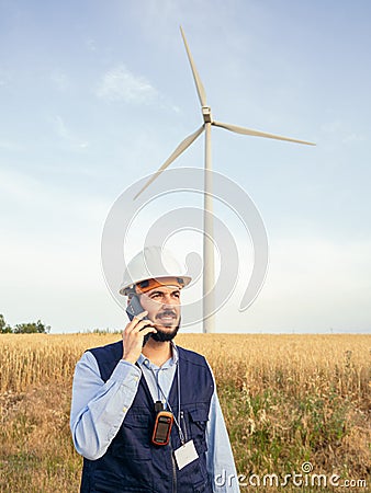 Detail of a male wind engineer with a safety helmet talking on the phone in a field of windmills. Renewable energy Stock Photo