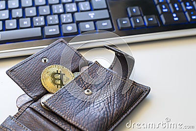 Detail of an open leather wallet with a big golden Bitcoin, fiat notes and credit cards and blue lit keyboard in Editorial Stock Photo