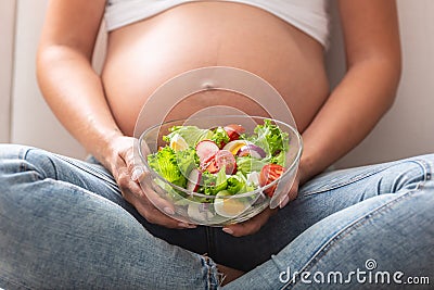 Detail of a pregnant woman sitting with a fresh salad bowl in her lap Stock Photo