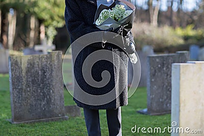 Close Up Of Senior Woman With Flowers Standing By Grave Stock Photo