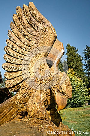 Detail shot of wooden sculpture of bird of prey with trees and blue sky in the background. Editorial Stock Photo