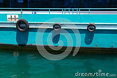 Detail of the side of a rusty old ferry boat of turquoise color with water reflection. Stock Photo