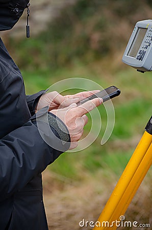 detail of a surveyor's hands configuring the total station with the mobile phone, topography works Stock Photo