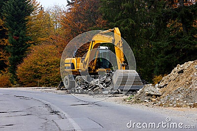 Detail view of a big excavator used to destroy old asphalt road on a mountain road. Stock Photo