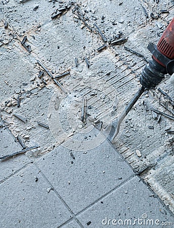 Construction worker using a handheld demolition hammer and wall breaker to chip away and remove old floor tiles during renovation Stock Photo